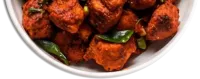 Crispy red fried chicken with curry leaves and green chillies on a white plate
