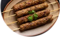 Seekh kebabs on wooden skewers with fresh coriander, on a round plate